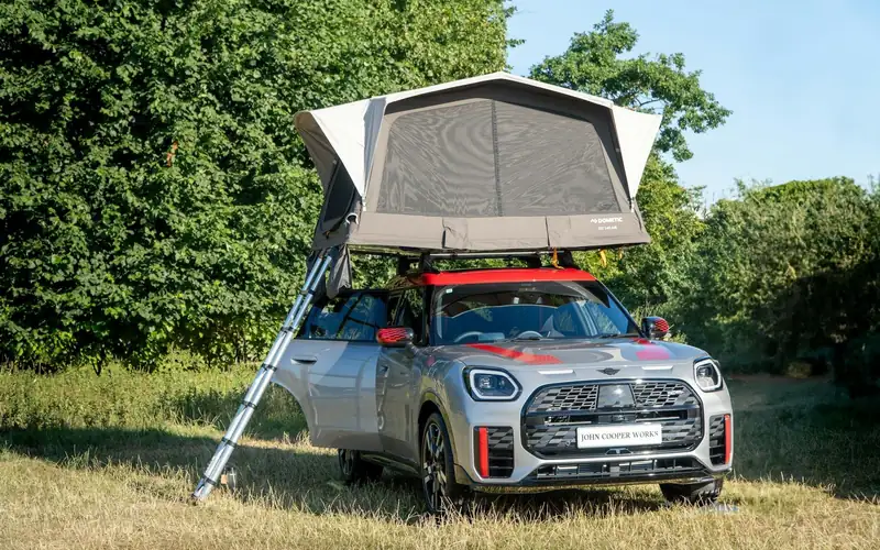 Kleine SUV met een uitgeklapte daktent en ladder op een grasveld