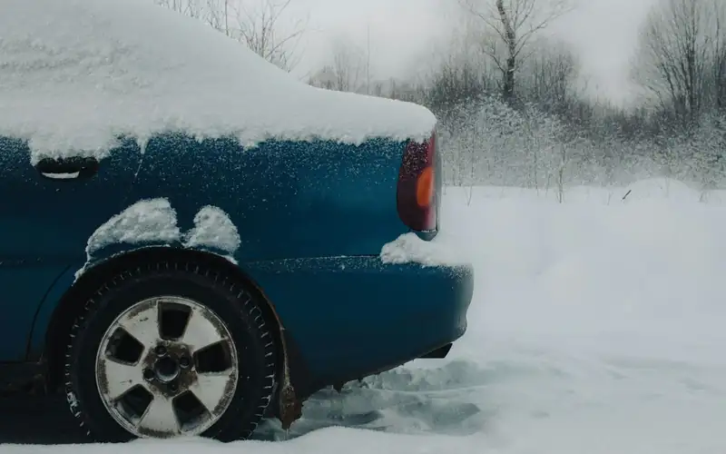 Achterwiel van een besneeuwde blauwe auto in verse sneeuw